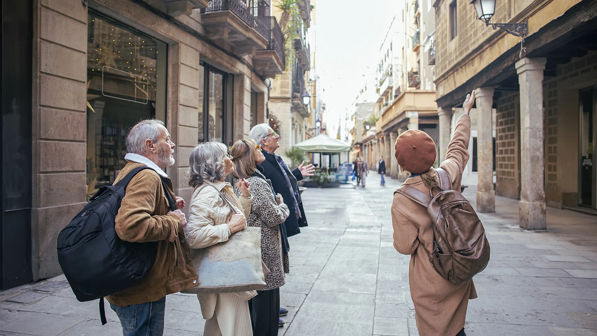 A tour guide in a rust-coloured beret points at a building while four tourists look up, in a narrow old-town street.