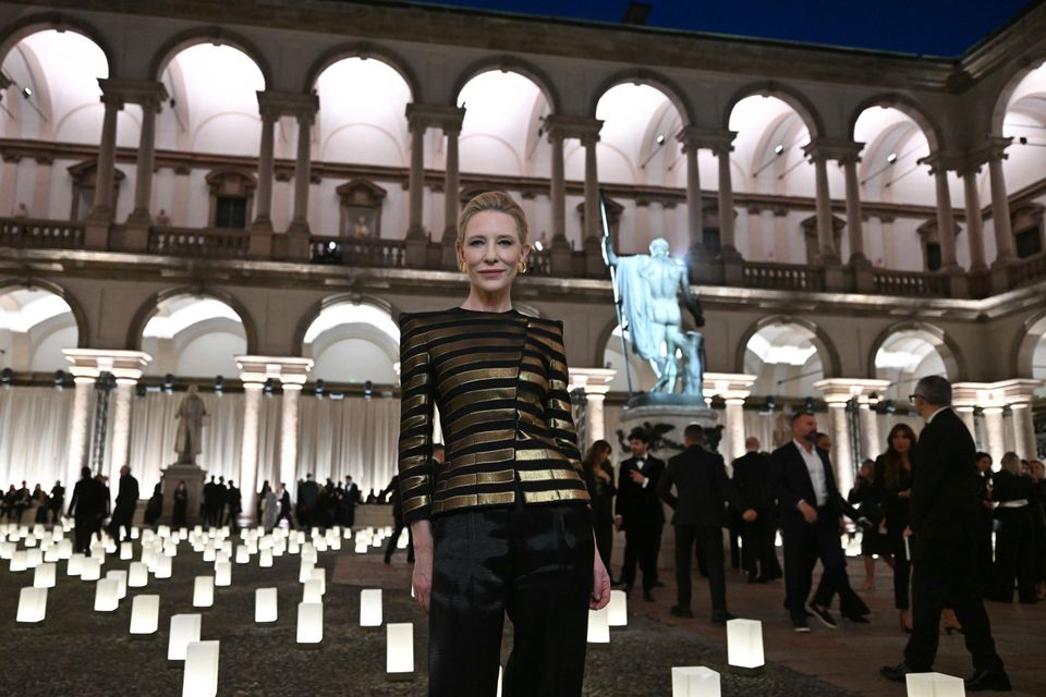 A woman in a gold-and-black striped Armani jacket in a candlelit arcaded courtyard at night.
